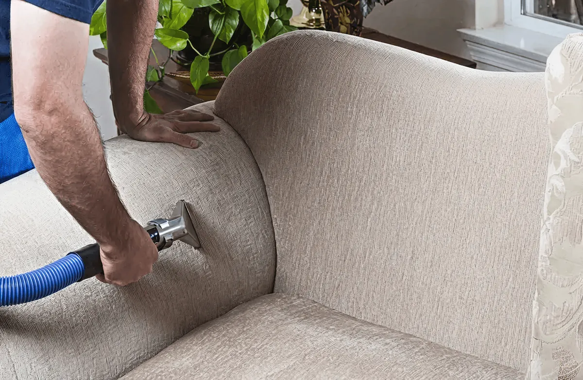 Professional upholstery cleaner deep-cleaning a fabric sofa with a handheld extraction tool and hose, Mesa, AZ.